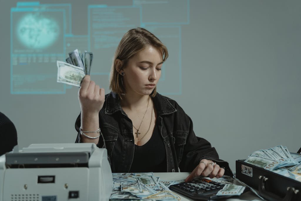 Young woman counting cash using a calculator in an office setting, surrounded by money.